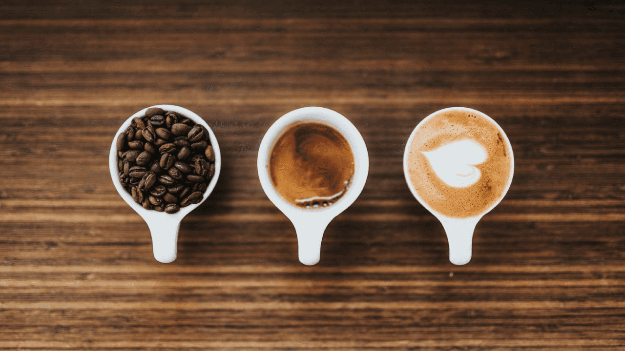 Top view of 3 cups of coffee on breakfast table one cup with coffee beans, one with a design on the latte and anotehr freshly brewed