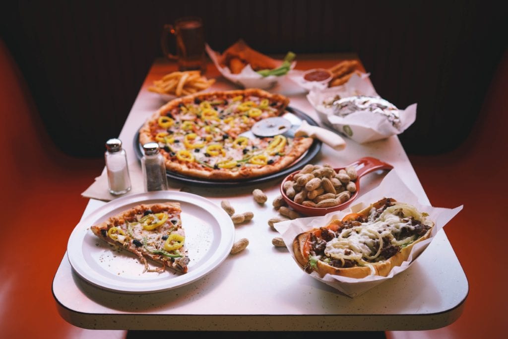 Booth in a restaurant with white table with a pizza buffalo wings salt and peper and peanutes