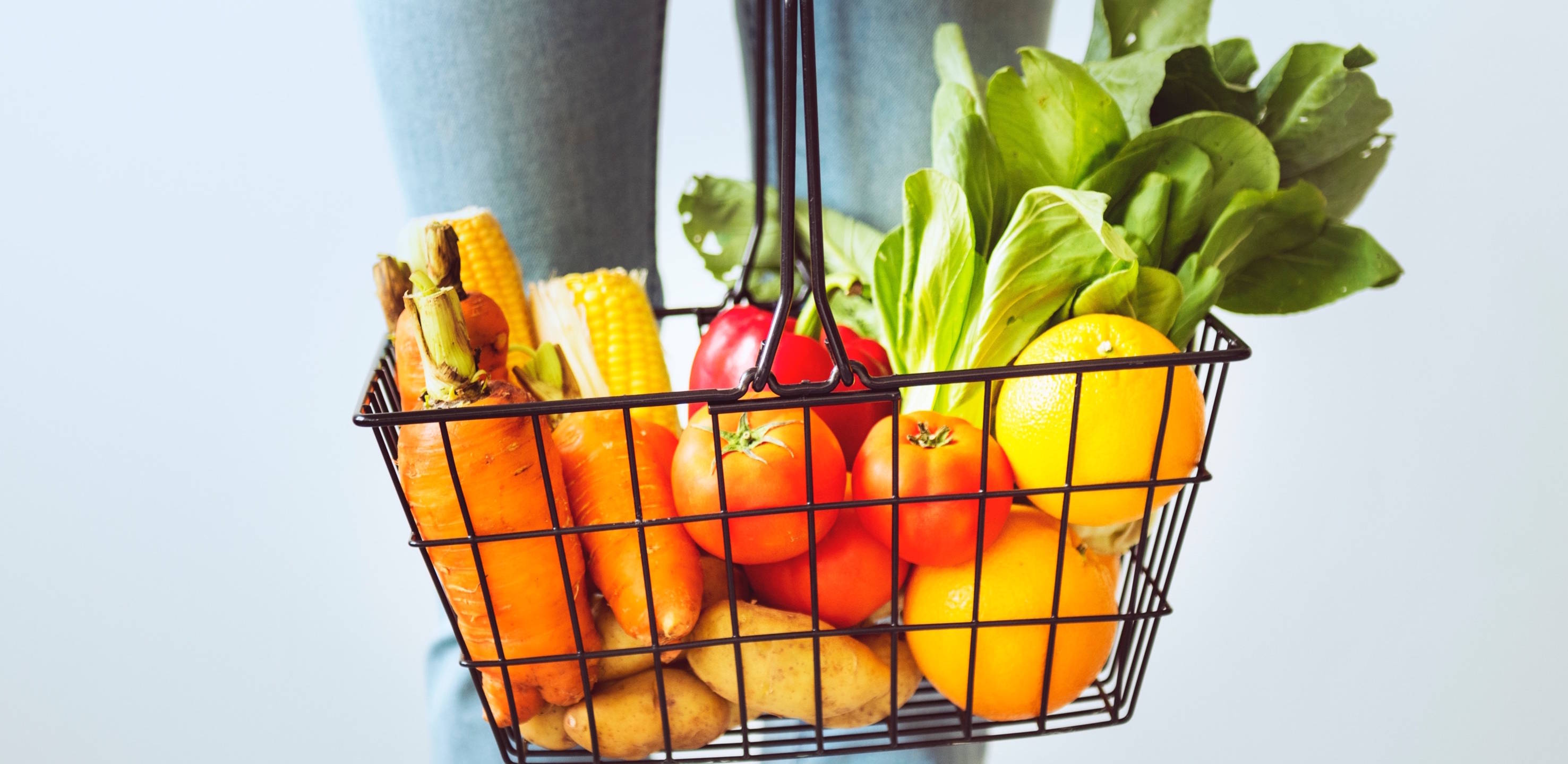 Close up view of black wire basket with whole carrots, corn, tomatoes potatoes and other vegetables.