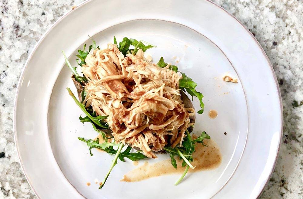 White glass plate with chicken salad on it sitting on light marble table