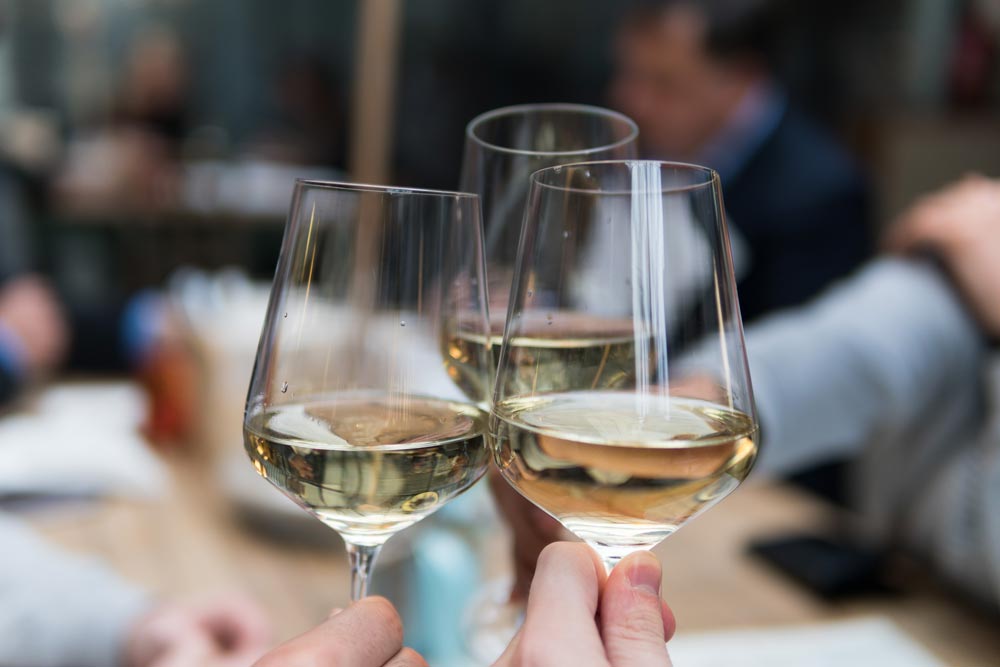 Three wine glasses toasting in restaurant with white wine.