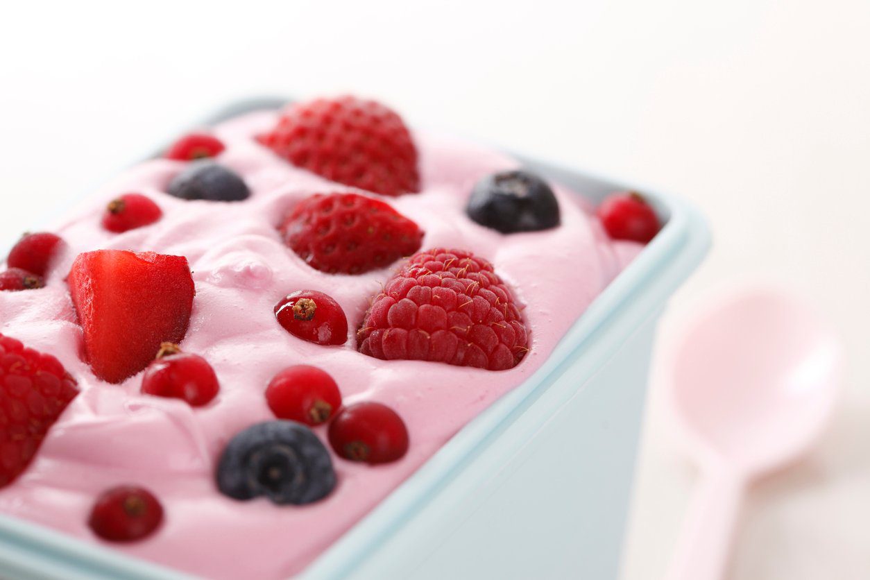 White container with blueberries, strawberries and raspberries in pink yogurt.