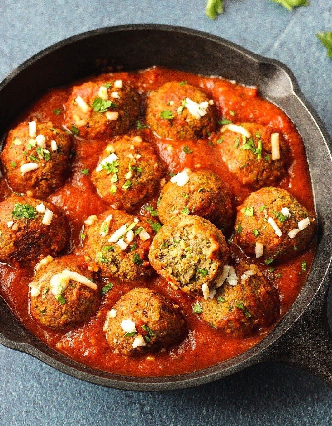 Black cast-iron skillet with meatball sitting in marinara sauce.