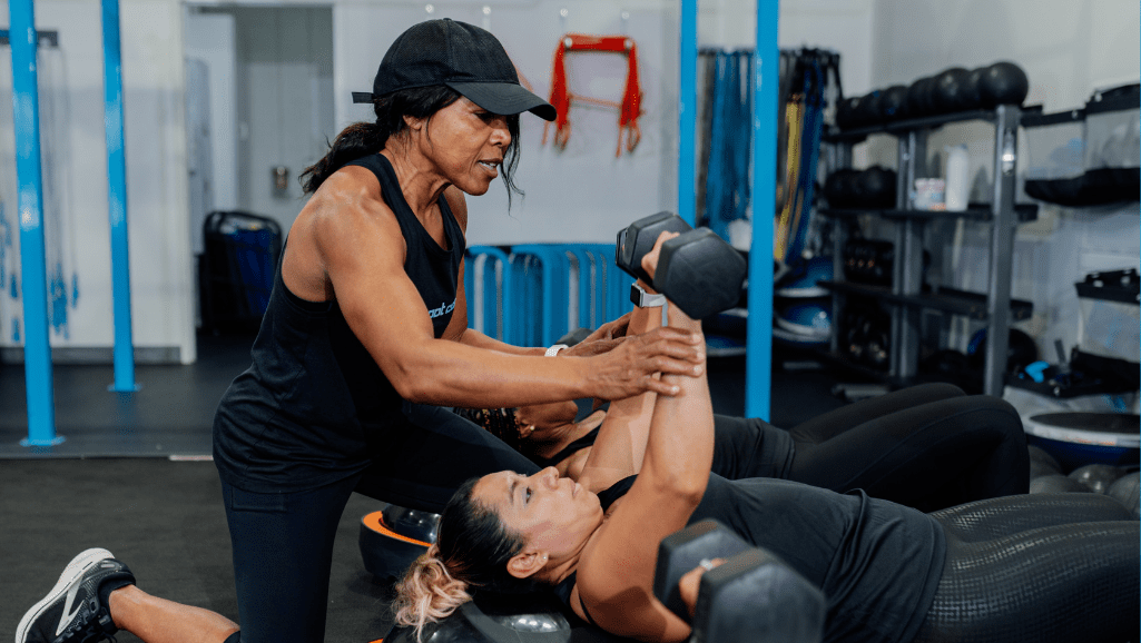 A Trainer is assisting a Member who is lifting heavy weights during a chest press strength training workout.